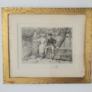Könnte beinhalten: Ein gerahmter Schwarzweißdruck eines Paares, das an einer Steinmauer steht. Der Mann hält einen Spazierstock und die Frau einen Korb. Der Druck ist vor einem weißen Hintergrund.
