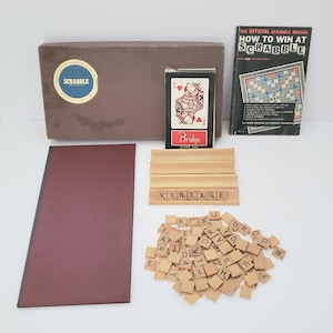 May include: Vintage Scrabble game set with a brown box, a wooden rack, a score pad, and letter tiles. The box has the word "SCRABBLE" printed on it. The score pad has the word "Bridge" printed on it. The wooden rack has the word "VINTAGE" spelled out with letter tiles.