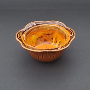 May include: A decorative ceramic bowl with a scalloped rim and a brown exterior. The interior features a vibrant orange and yellow design. The bowl's design includes a repeating pattern of vertical lines.