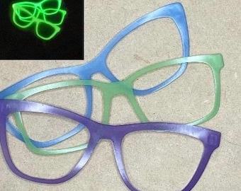 May include: Three pairs of eyeglasses in different colors: purple, blue, and green. The eyeglasses are stacked on top of each other.