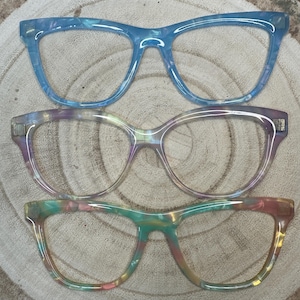 May include: Three pairs of colourful eyeglasses with a marbled pattern. The top pair is light blue, the middle pair is purple and the bottom pair is green, yellow, and pink.