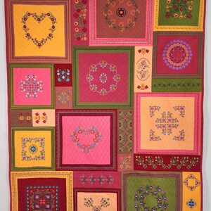 May include: A quilt with a patchwork design featuring various floral patterns in shades of red, pink, yellow, and green. The quilt is made up of squares and rectangles, each with a different design. The quilt is hanging on a wall.