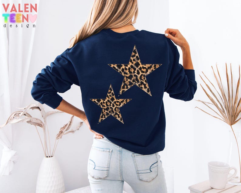 May include: Navy blue sweatshirt featuring two leopard print stars on the back. The sweatshirt has long sleeves and a crew neck. The VALEN TEEN design logo is visible in the upper left corner.