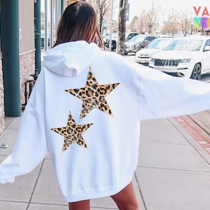 May include: White hoodie with a hood and long sleeves. The back of the hoodie features two leopard print stars. The hoodie is a casual style, suitable for everyday wear. The brand name "VALENTEEN" is visible in the background.