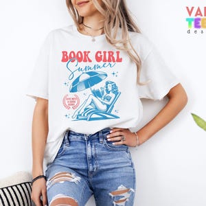 May include: White t-shirt with the text "BOOK GIRL Summer" in red and blue. The graphic features a woman reading under a beach umbrella. The shirt also has the text "Dive into a good book!" in a circular design.