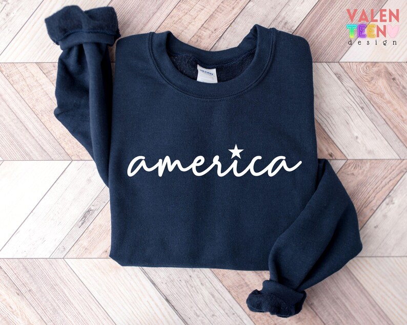 Puede incluir: Sudadera azul marino con la palabra "america" en escritura blanca, con una estrella sobre la "i". La sudadera tiene cuello redondo y mangas largas con pu&ntilde;os acanalados. La marca "VALENTEEN design" est&aacute; impresa en la esquina superior derecha.