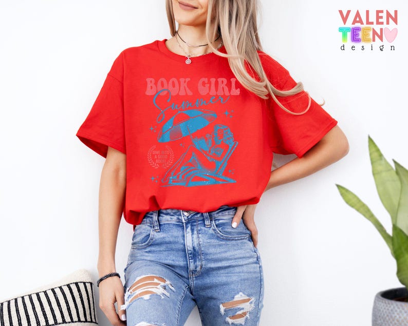 May include: A red t-shirt with a blue graphic that reads "BOOK GIRL Summer". The graphic depicts a person relaxing in a beach chair under an umbrella. The shirt is paired with blue jeans.