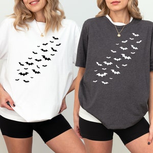 May include: Two people wearing t-shirts with a black bat design. The shirts are white and gray. The bats are arranged in a diagonal line from the shoulder to the hip.