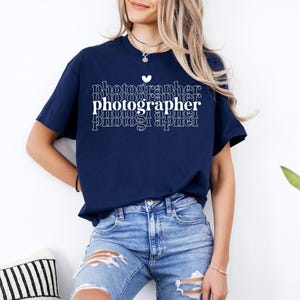 May include: A navy blue t-shirt with a white graphic that says "photographer" in a stacked, repeating pattern. A small white heart is above the word "photographer".