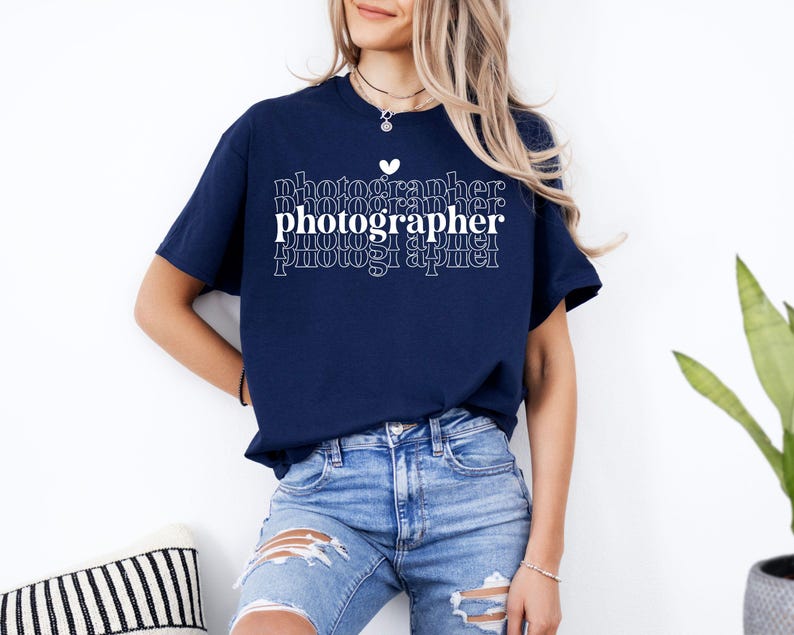 May include: A navy blue t-shirt with a white graphic that says "photographer" in a stacked, repeating pattern. A small white heart is above the word "photographer".