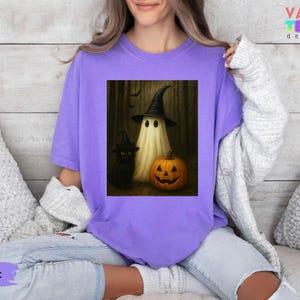 Puede incluir: Camiseta violeta con un dise&ntilde;o de Halloween. El dise&ntilde;o muestra un fantasma con un sombrero de bruja, un gato negro y una calabaza tallada. La camiseta tiene un corte holgado y est&aacute; hecha de un material suave.