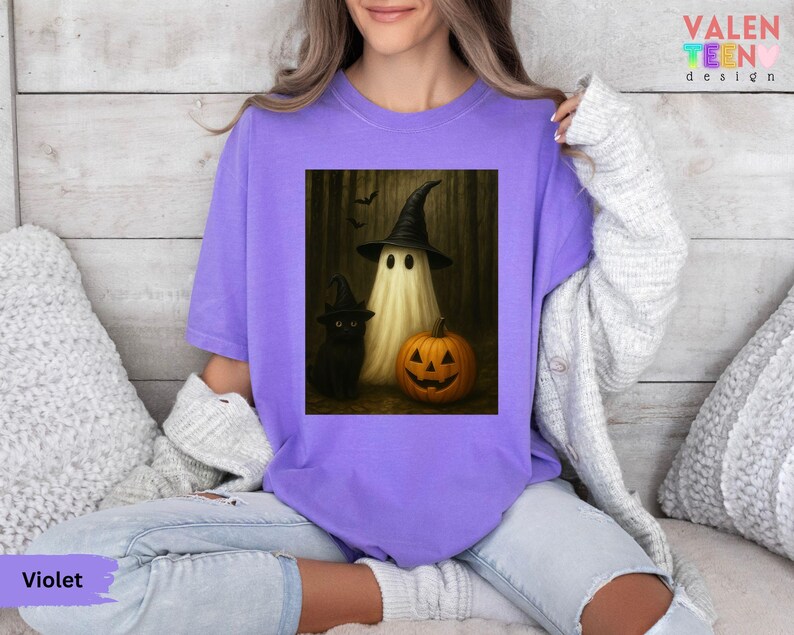 Puede incluir: Camiseta violeta con un dise&ntilde;o de Halloween. El dise&ntilde;o muestra un fantasma con un sombrero de bruja, un gato negro y una calabaza tallada. La camiseta tiene un corte holgado y est&aacute; hecha de un material suave.