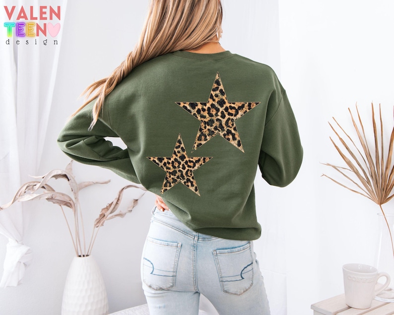 May include: An olive green sweatshirt featuring two leopard print stars on the back. The sweatshirt has long sleeves and a crew neck. The text "VALEN TEEN design" is visible in the upper left corner.