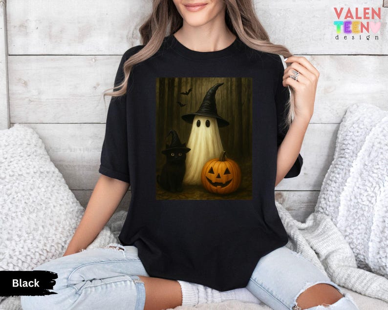 Puede incluir: Camiseta negra con un dise&ntilde;o de Halloween. El gr&aacute;fico muestra un fantasma con sombrero de bruja, un gato negro y una calabaza tallada. La camiseta tiene la palabra "Black" en la parte inferior.