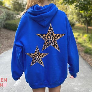 May include: A royal blue hoodie with two leopard print star designs on the back. The hoodie has a hood and long sleeves. The text "VALEN TEEN design" is visible in the lower left corner.