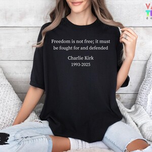May include: Black t-shirt with the quote "Freedom is not free; it must be fought for and defended" and the name "Charlie Kirk 1993-2025" in white text. The shirt is a crew neck style.