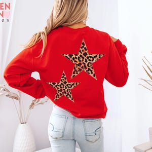 May include: A red sweatshirt with two leopard print star designs on the back. The sweatshirt has long sleeves and a crew neck. The text "VALEN TEEN design" is visible in the upper left corner.