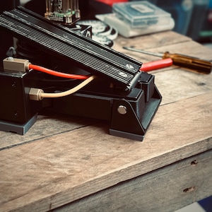 May include: A black foot pedal with a textured surface and a red and yellow cable attached. The pedal is on a wooden surface.