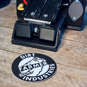 May include: A black and white sticker with the text "Dirt Farmer Industries" and a white polar bear graphic. The sticker is on a wooden surface.