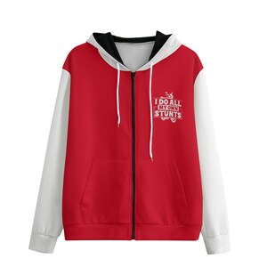 May include: Red zip-up hoodie with white sleeves and a black-lined hood. The front features a white graphic that reads "I DO ALL MY OWN STUNTS" with a motorcycle illustration. The hoodie has a front pocket and white drawstrings.