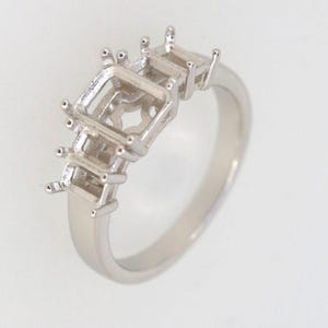 May include: A silver-toned metal ring setting featuring three empty rectangular prongs designed to hold gemstones. The band is smooth and polished, with a central larger rectangular setting flanked by two smaller rectangular settings on each side.
