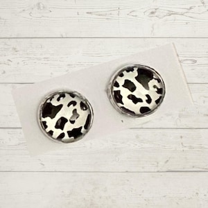 May include: A pair of silver stud earrings with a black and white cow print design.