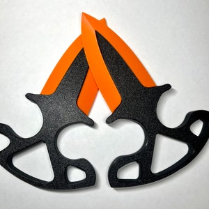 Puede incluir: Dos cuchillos de lanzamiento negros con mangos naranjas. Los cuchillos están cruzados en forma de X.