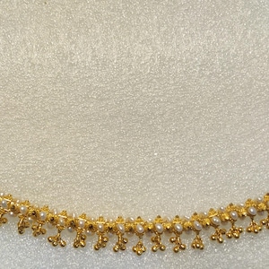 Puede incluir: Un collar de oro con una cadena delicada y pequeños detalles de perlas. El collar tiene un diseño sencillo con una fila de perlas y pequeños colgantes de oro.