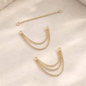 May include: Three gold-toned metal chain connectors for jewelry making. One piece is a single straight chain, one is a double-layered draped chain, and one is a triple-layered draped chain. Each piece features small circular jump rings at both ends.