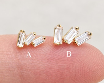 Könnte beinhalten: Zwei goldfarbene Ohrstecker mit klaren Baguette-Schliff-Steinen. Option A zeigt drei kleine Steine in einer Gruppe, während Option B zwei größere Steine nebeneinander angeordnet hat. Beide Designs sind mit den Buchstaben A und B gekennzeichnet.
