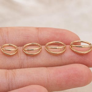 以下が含まれることがあります： ダブルバンドデザインが特徴の、小さな金色の円形リング4つ。リングは水平に一列に並べられており、磨かれた金属光沢と、一貫した均一な外観を持つシンプルなオープンループ構造を示しています。