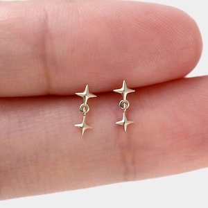 以下が含まれることがあります： 2つの4尖星が細い金属リンクで垂直に繋がれた、小さなゴールドトーンのスタッドピアス一対。星は光沢のある反射面を持ち、左右対称のデザインで、繊細でシンプルな外観を作り出しています。
