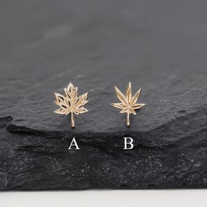 May include: Two gold-toned stud earrings shaped like leaves. The earring labelled A is a five-pointed maple leaf design, and the earring labelled B is a seven-pointed leaf design. Both earrings feature detailed cutouts and a polished metallic finish.