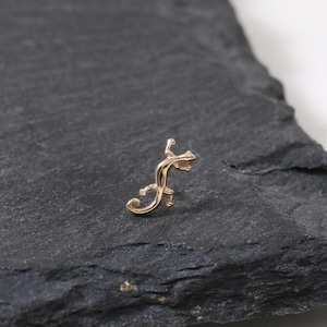 May include: A small, gold-colored initial letter "F" in a cursive script. The letter is placed on a dark gray, textured, rectangular surface with a white background.