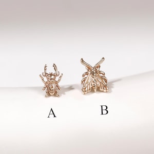 May include: Two small gold-toned metal insect-shaped charms or earrings. Item A is a beetle with detailed legs and antennae. Item B is a moth with spread wings and prominent antennae. Both pieces are labeled with black letters A and B below them.