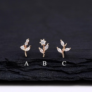 May include: Three gold-toned leaf-shaped earrings with clear crystal accents are displayed on a dark surface. Each earring has a different design, labeled A, B, and C. The earrings are delicate and elegant, suitable for various occasions.