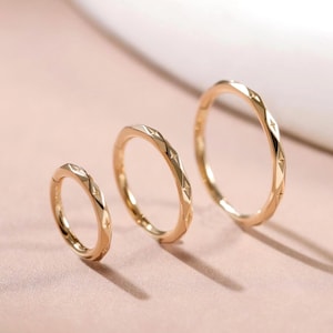 May include: Three gold-toned hoop rings arranged in a row from smallest to largest. Each ring features a delicate, repeating star-shaped pattern engraved along the outer surface, creating a subtle texture on the polished metal bands.