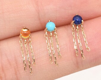 May include: Three gold stud earrings, each featuring a small round gemstone in orange, turquoise, or dark blue. Each earring has three delicate gold chains hanging from the base of the stone, creating a dangling effect on the earlobe.