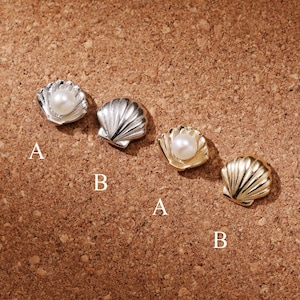 May include: Four shell-shaped stud earrings arranged in two pairs. One pair features a silver-tone shell with a white pearl and a plain silver-tone shell. The other pair features a gold-tone shell with a white pearl and a plain gold-tone shell. Each item is labelled with the letter A or B.