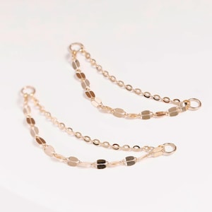 May include: Two delicate gold-toned jewelry chain connectors, each featuring a double-strand design. One strand consists of small circular links, while the other strand features flat, elongated oval links. Each end terminates in a small jump ring.