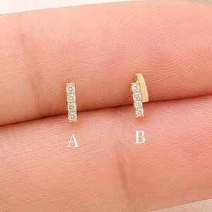May include: Two gold stud earrings with clear stones. Option A is a vertical bar with four small stones. Option B is a gold bar with two small stones set at an angle. Both earrings are displayed on a finger for scale and clarity.