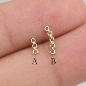 以下が含まれることがあります： 指の上に置かれた2つの小さな金色の金属製チェーンパーツ。Aとラベル付けされたパーツは2つの円形リンクで構成され、Bとラベル付けされたパーツは4つの円形リンクで構成されています。どちらのパーツも細く繊細で、金属光沢のある金色をしています。
