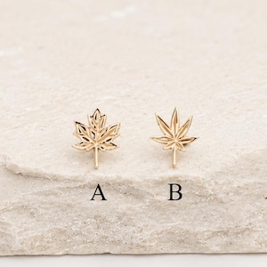 Peut inclure: Deux boucles d'oreilles à clous dorées en forme de feuilles. La boucle d'oreille étiquetée A présente un motif de feuille d'érable à cinq pointes, tandis que la boucle d'oreille B présente un motif à sept pointes. Finition métallique polie.