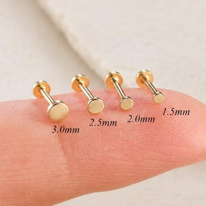May include: Four gold-tone flat-back stud earrings with circular tops, arranged by size. The labels indicate diameters of 3.0mm, 2.5mm, 2.0mm, and 1.5mm. Each stud features a thin post and a small, smooth, round disc head in a polished gold finish.