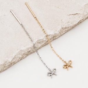 May include: Two threader earrings, one in silver tone and one in gold tone, each featuring a delicate chain that ends in a small, dainty bow charm. The earrings are designed to be pulled through the earlobe, showcasing a minimalist aesthetic.