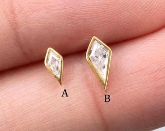 Könnte beinhalten: Zwei goldfarbene Ohrstecker mit klaren, drachenförmigen Steinen in Metallfassungen. Der kleinere Ohrstecker ist mit A und der größere mit B gekennzeichnet. Beide Ohrringe haben ein spitz zulaufendes, geometrisches Design.
