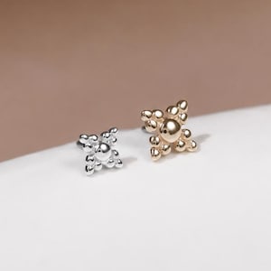 May include: Two small stud earrings, one in a polished silver tone and one in a warm gold tone. Each earring features a central circular bead surrounded by four smaller beads arranged in a cross-like pattern, creating a cluster design.