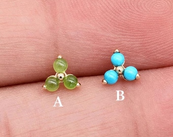 May include: Two gold stud earrings, each featuring three small round gemstones arranged in a triangular cluster. The earring labeled A has light green stones, while the earring labeled B has bright turquoise blue stones.