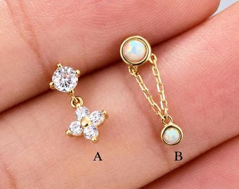 May include: Two gold-tone earrings labeled A and B. Earring A features a single round clear stone above a four-stone flower-shaped cluster. Earring B consists of a round opal-like stone connected by two delicate gold chains to a smaller matching stone.
