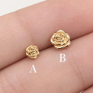 Puede incluir: Dos pendientes de botón de metal en tono dorado con forma de pequeñas rosas. El pendiente etiquetado como A es más pequeño que el pendiente etiquetado como B. Ambas piezas presentan un diseño de pétalos en espiral con acabado pulido.